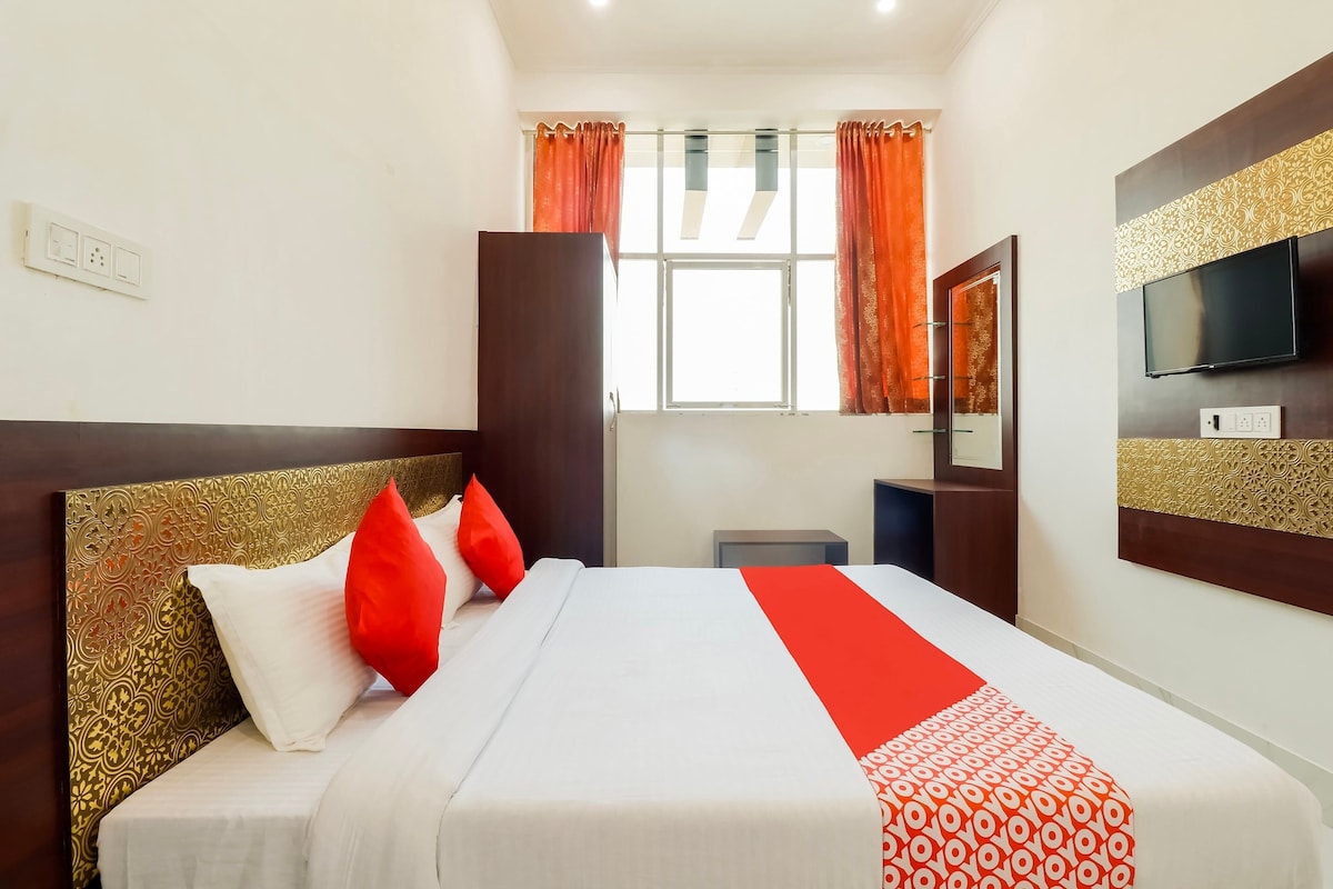 A hotel room with a bed, a TV, a window with curtains, and a mirror.
