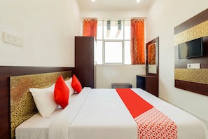 A hotel room with a bed, a TV, a window with curtains, and a mirror. - Hotel O Subham Residency (Bikaner)