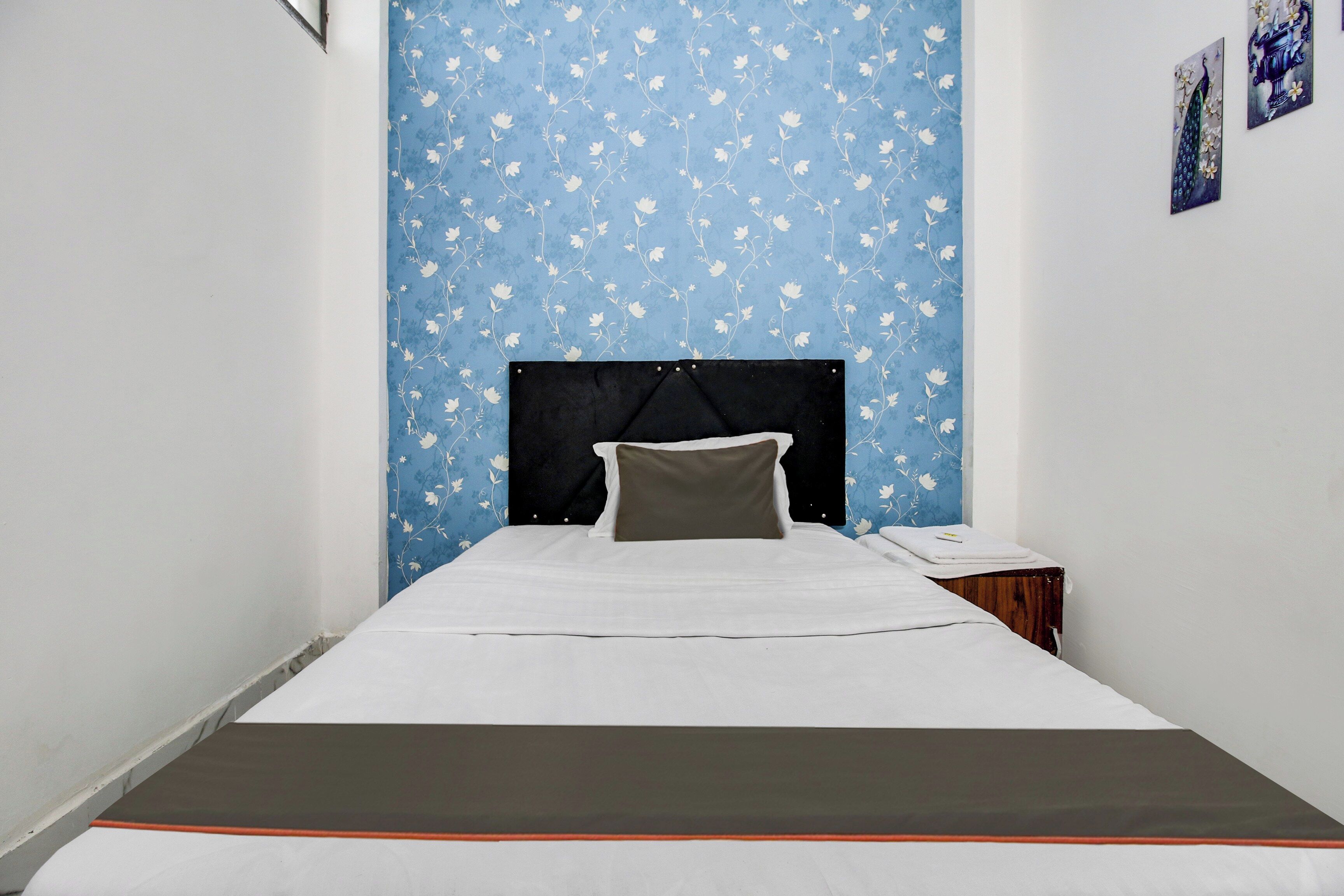 A single bed with a black headboard, white bedding, and a grey pillow in a room with blue floral wallpaper.