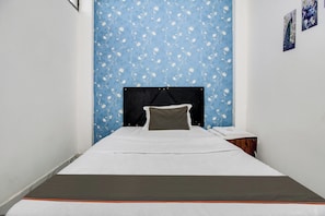Ein Einzelbett mit schwarzem Kopfteil, weißer Bettwäsche und einem grauen Kopfkissen in einem Zimmer mit blauem Blumenwallpaper.