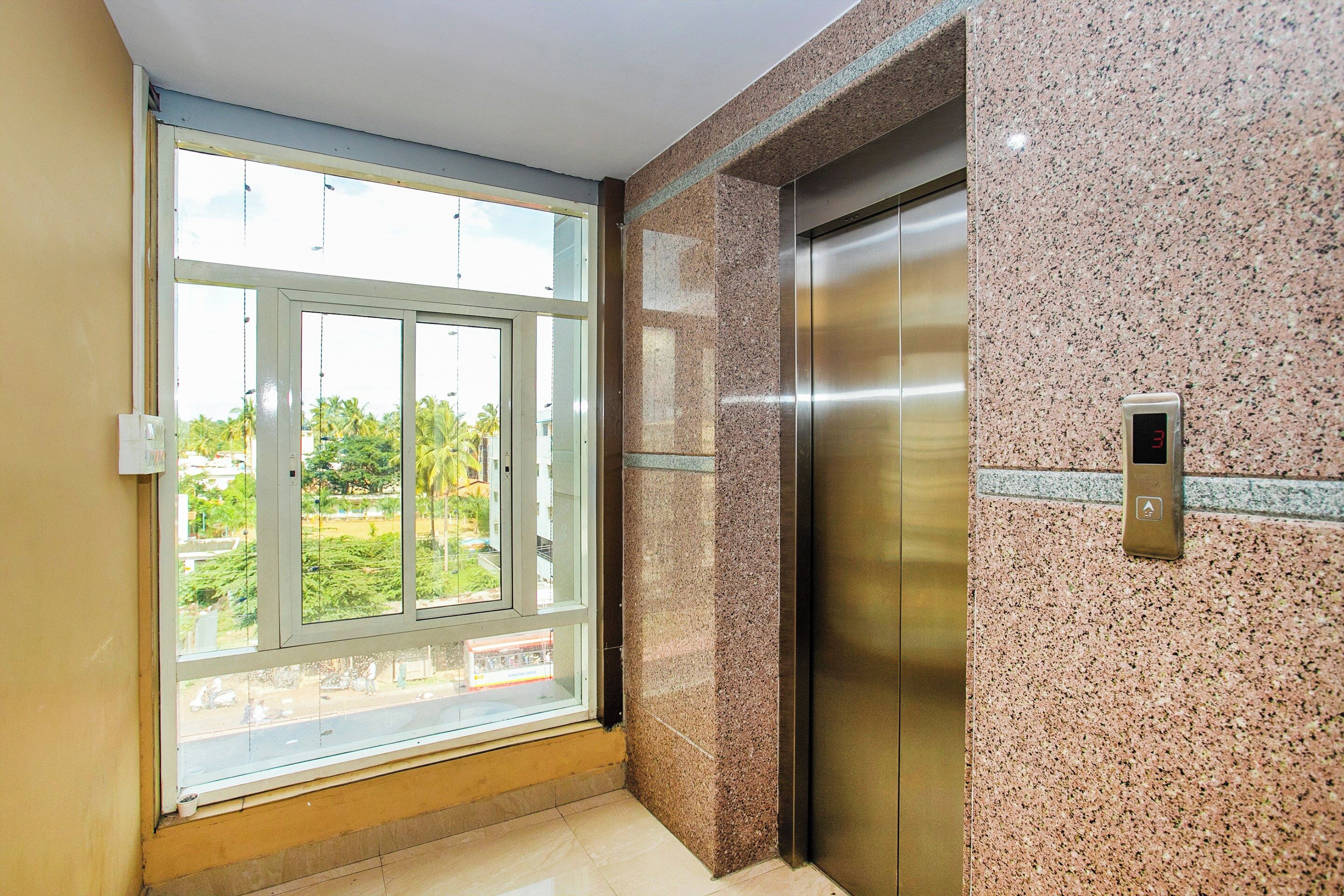 A room with a large window, an elevator, and a wall with a textured pattern.