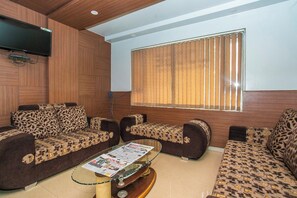 A living room with patterned sofas, a coffee table with newspapers, and a television mounted on the wall. - Hotel O White Fort Near Lalbagh (Bangalore)