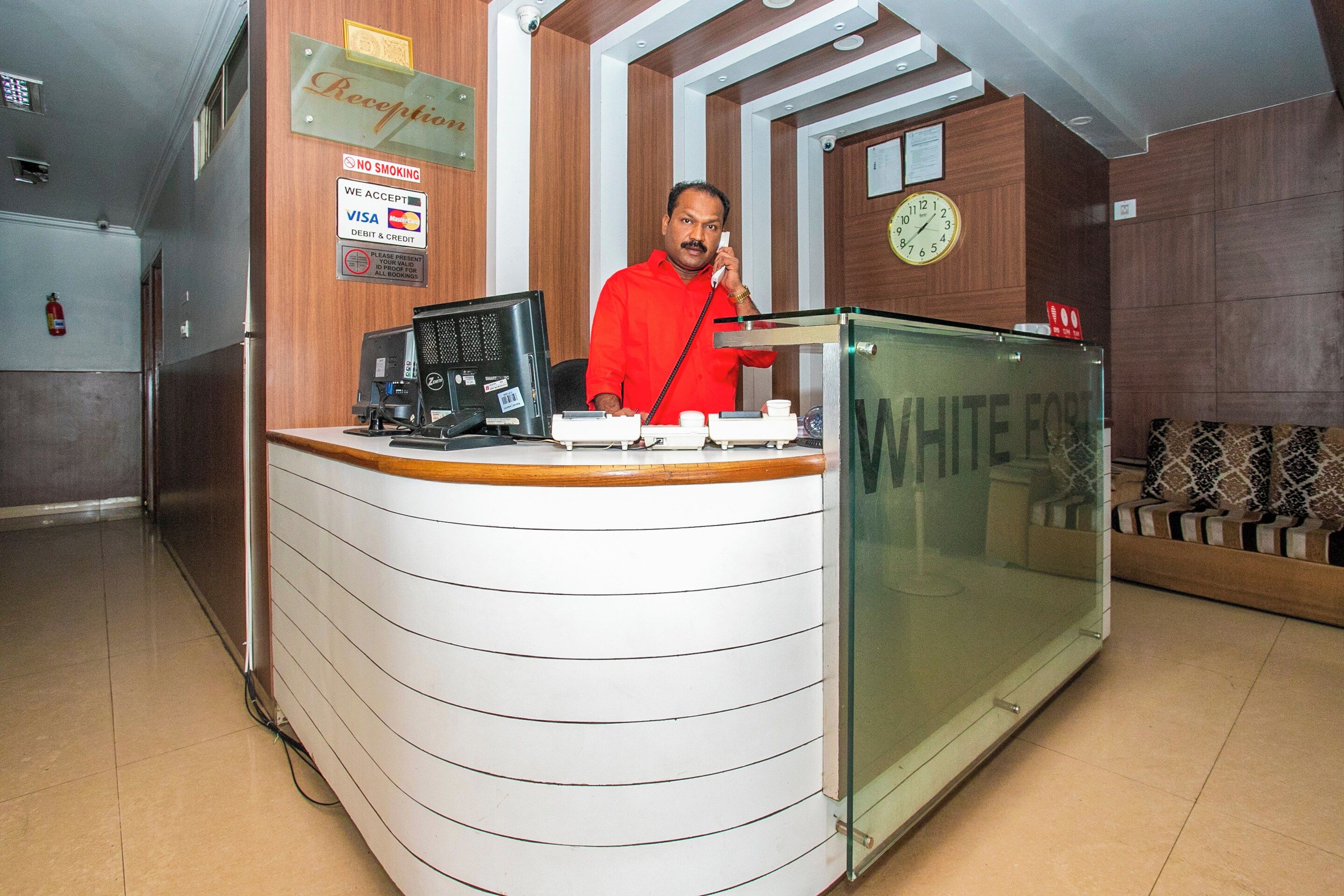 A reception desk with a glass partition, a clock, and a sign indicating no smoking.