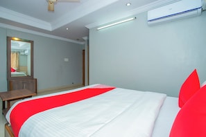A hotel room with a bed, a mirror, a bedside table, an air conditioning unit, and a ceiling fan. - Hotel O White Fort Near Lalbagh (Bangalore)