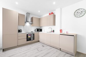 Une cuisine moderne avec des meubles de couleur beige, une hotte en acier inoxydable, un four à micro-ondes, une bouilloire et un évier.