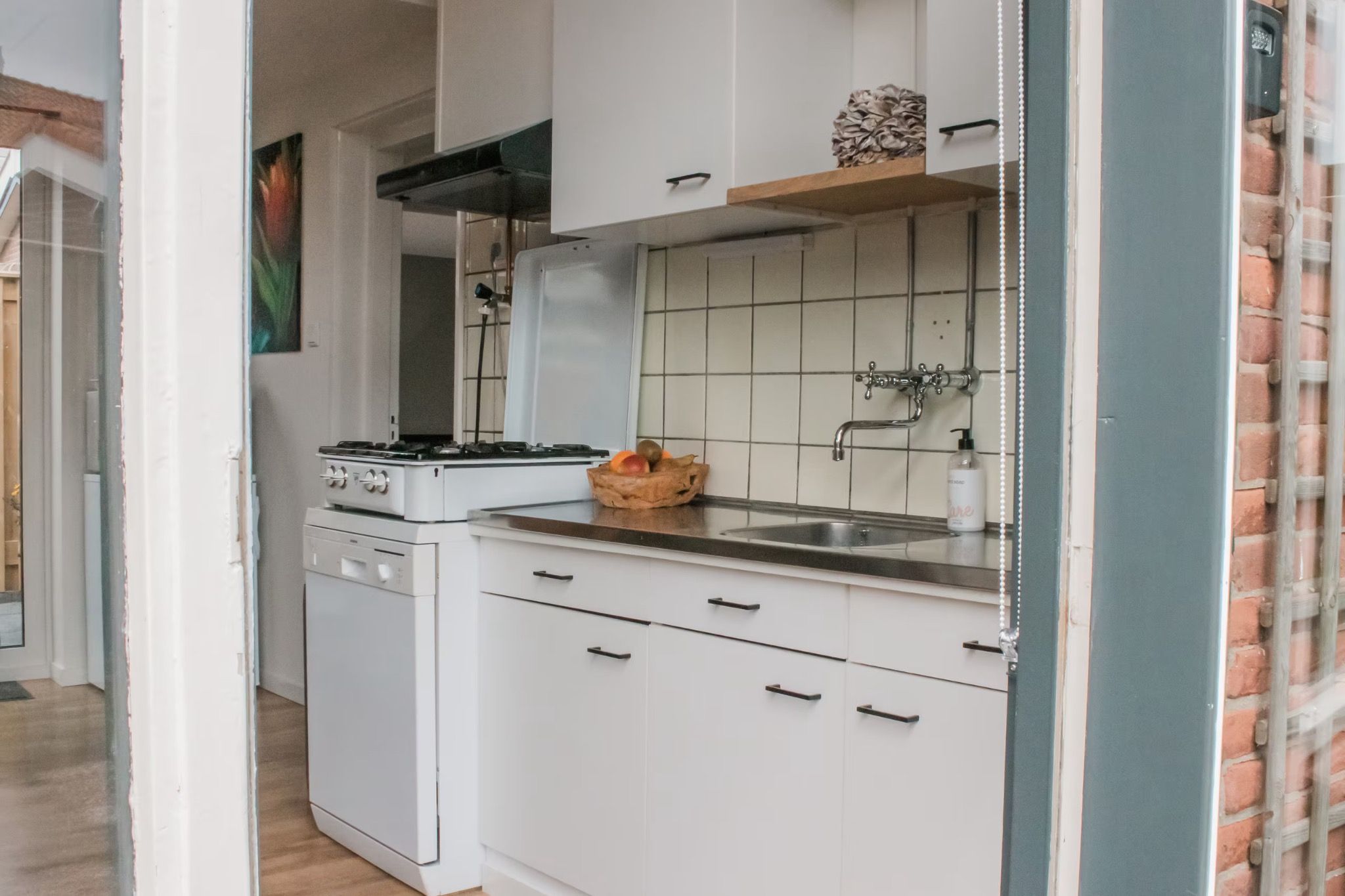 Une cuisine avec des meubles blancs, une cuisinière, un évier et un panier de fruits posé sur le comptoir.