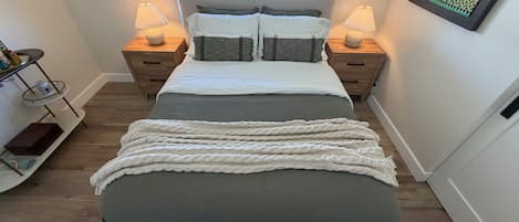 A bedroom with a bed, two bedside tables, a window, and a wall-mounted artwork.