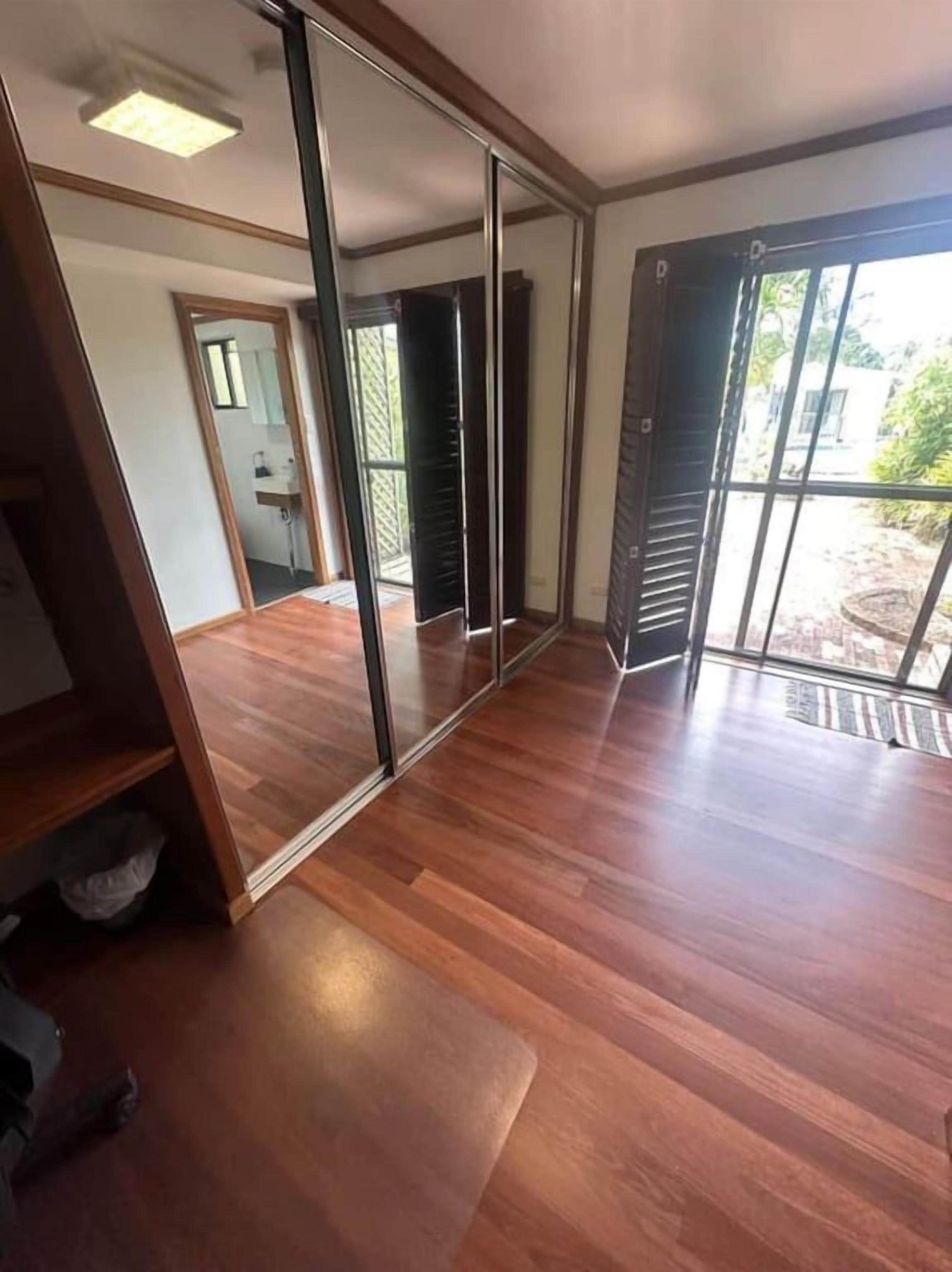 A room with a sliding glass door leading to an outdoor area, a wooden floor, and a visible bathroom with a shower.