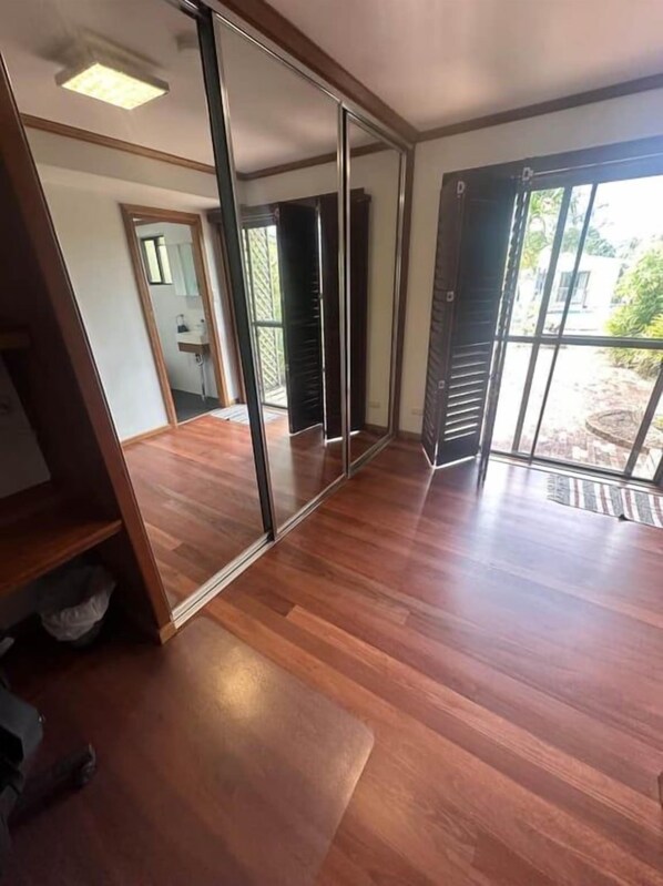 Habitació amb porta corredissa de vidre que dona a zona exterior, sòl de fusta i bany visible amb dutxa.