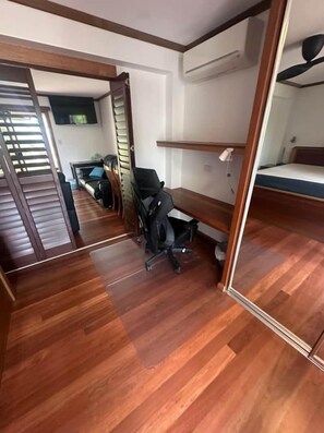 Una habitació amb terra de fusta, un escriptori amb una cadira, un llit superposat i un mirall.