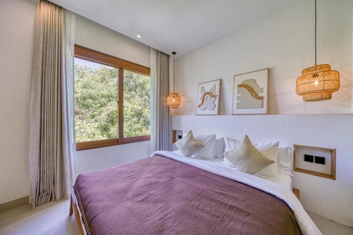 A bedroom with a large bed, a window with curtains, and wall-mounted artwork.