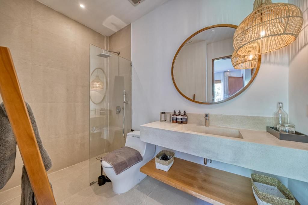 A modern bathroom with a glass shower enclosure, a white sink with a wooden vanity, and a large mirror with a circular frame.