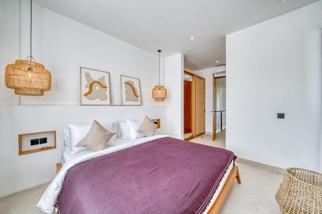 A bedroom with a large bed, two wall-mounted lamps, and a door leading to another room.