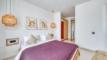 A bedroom with a large bed, two wall-mounted lamps, and a door leading to another room.