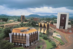 Un edificio moderno con un diseño geométrico singular, rodeado de abundante vegetación y otras construcciones contemporáneas.