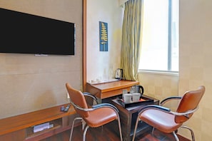A hotel room with a TV mounted on the wall, a wooden desk with a coffee maker, two leather chairs, and a window with curtains. - Palette Hotel by CheckIn Zero Mile (Nagpur)