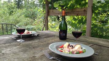 A wooden table with two plates of food and two glasses of red wine, a bottle of wine, and a fork.