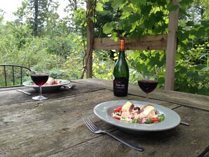 A wooden table with two plates of food and two glasses of red wine, a bottle of wine, and a fork.