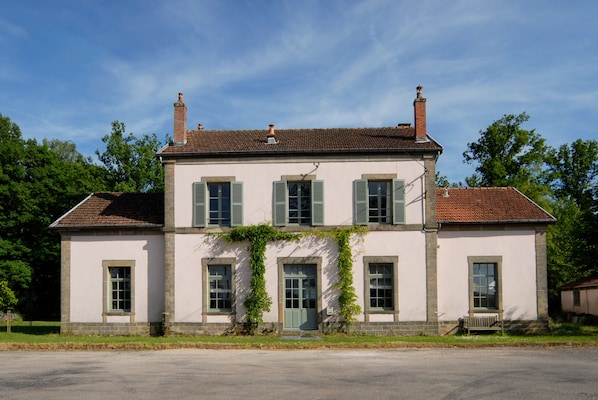 A two-story building with a symmetrical facade, featuring a central entrance with a green door, flanked by windows with shutters.