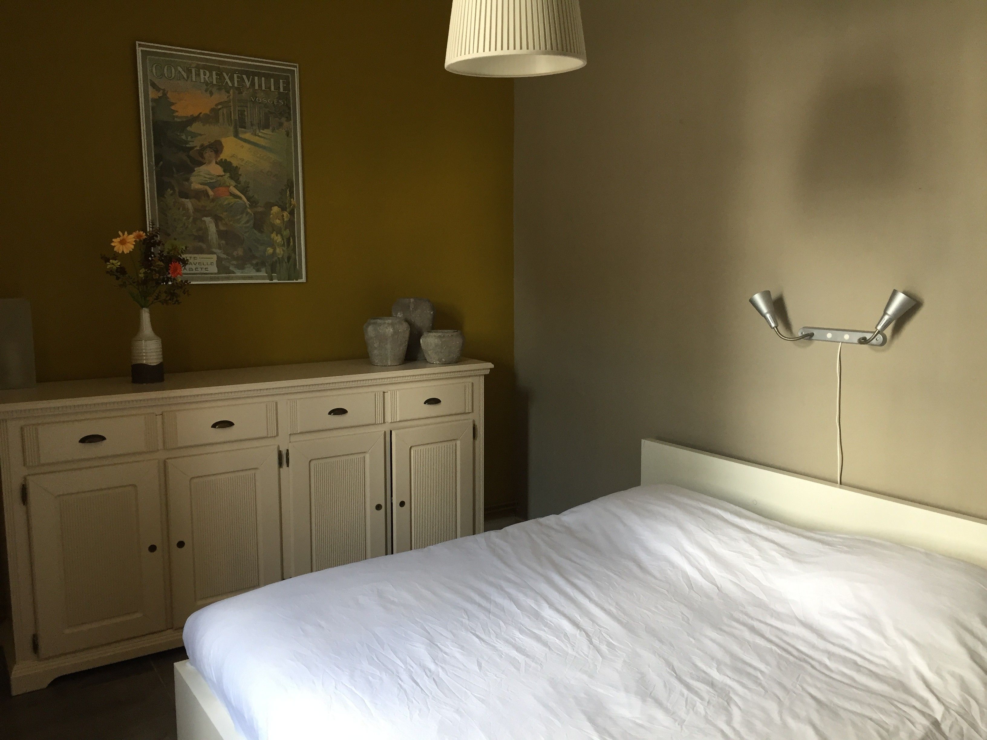 Een slaapkamer met een bed, een kapstok, een wandlamp en een poster.