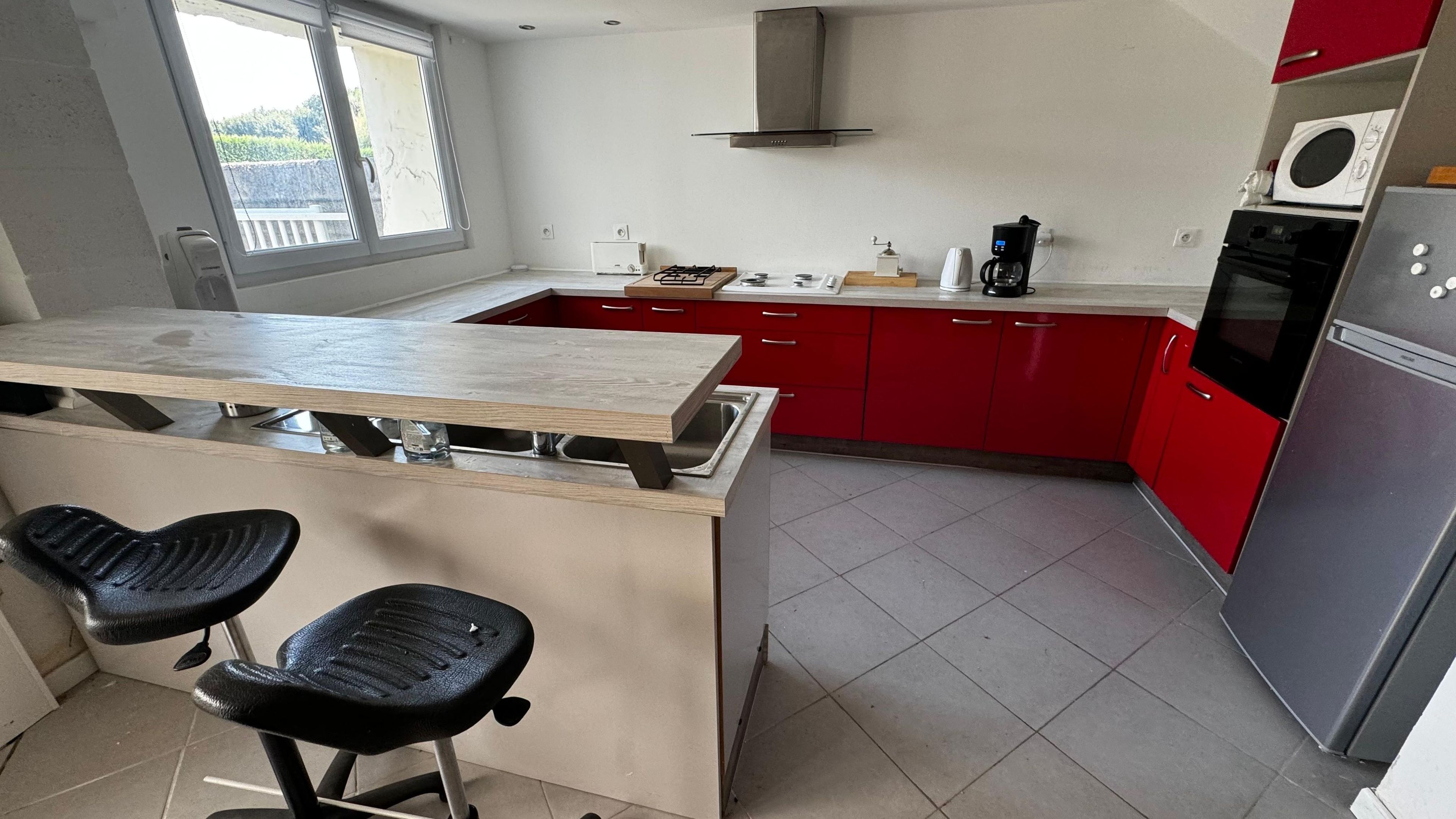 A kitchen with a central island, red cabinets, a stainless steel refrigerator, and a microwave.