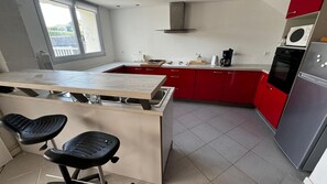 A kitchen with a central island, red cabinets, a stainless steel refrigerator, and a microwave.