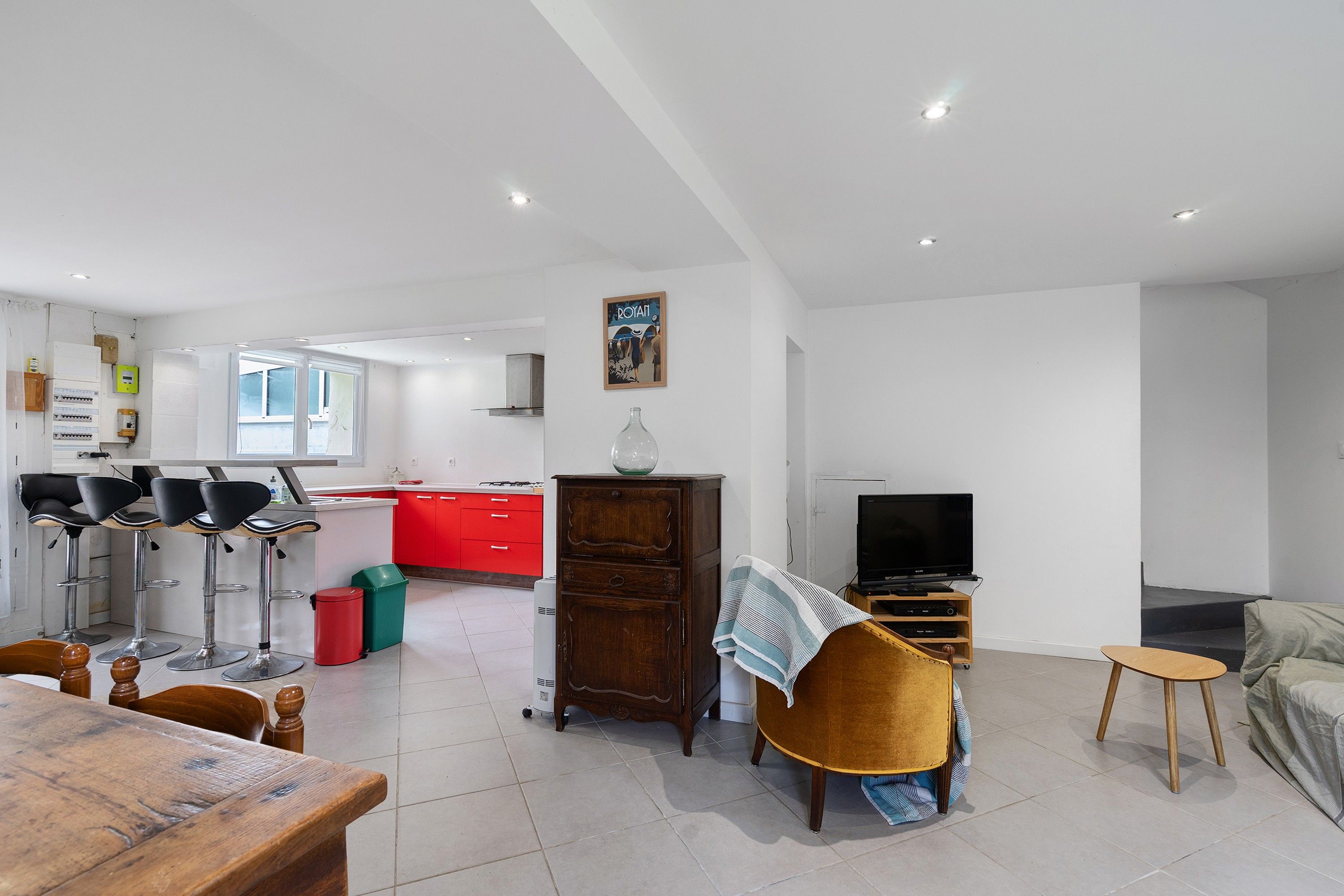A modern living room with a dining area, a kitchen with red cabinets, and a television.