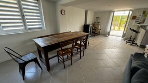 A dining area with a wooden table and chairs, a clock on the wall, and a view through a glass door to the outside. - Holiday Home 'De Plein Pied Avec Jardin' with Shared Terrace, Private Garden and Wi-Fi (Chaillevette)