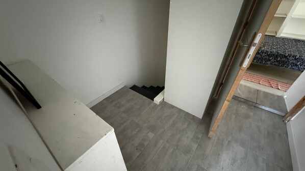 Un couloir étroit avec un cadre de porte en bois, un mur blanc et un sol recouvert de moquette.