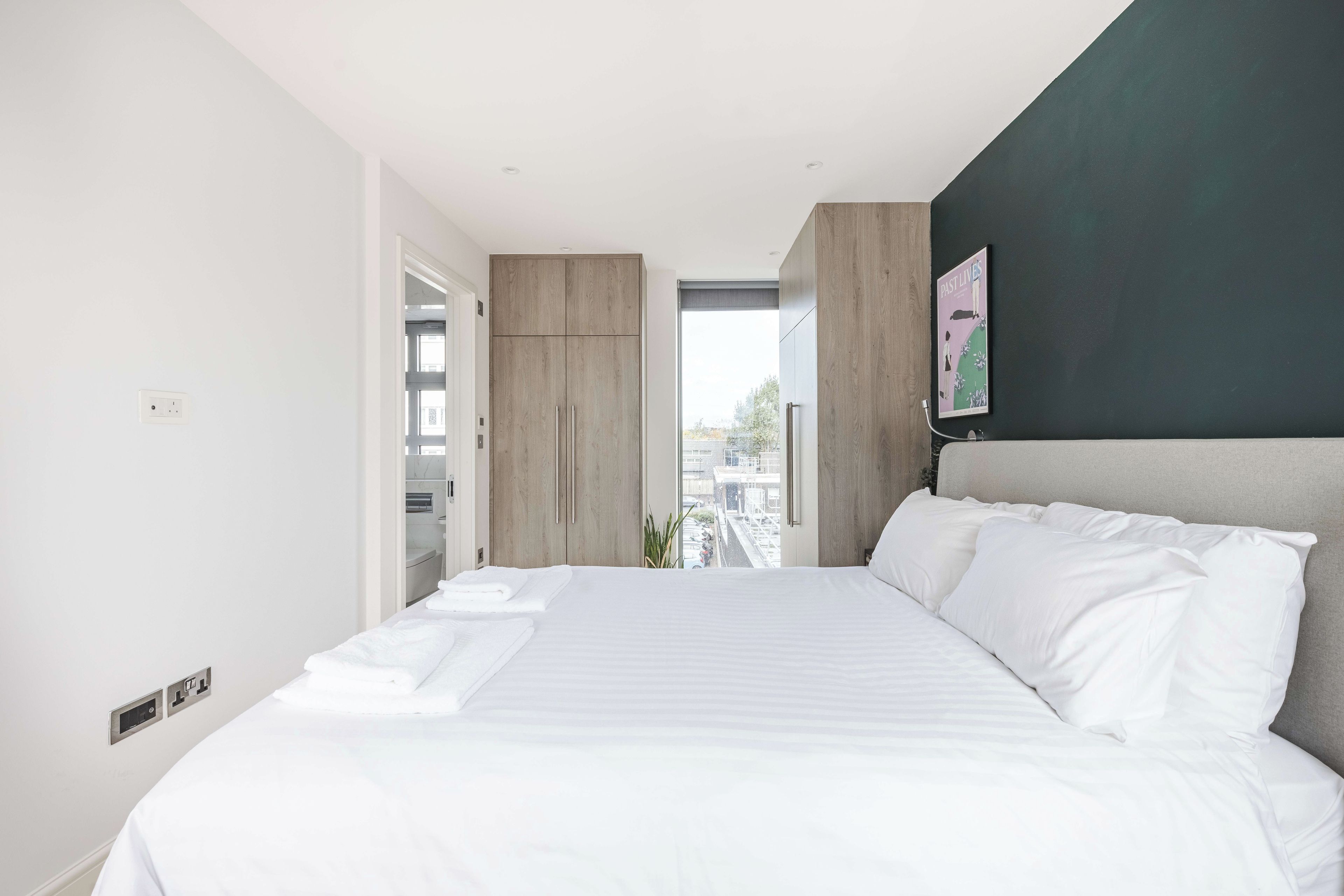 A modern bedroom with a large bed, a view through an open door, and a painting on the wall.