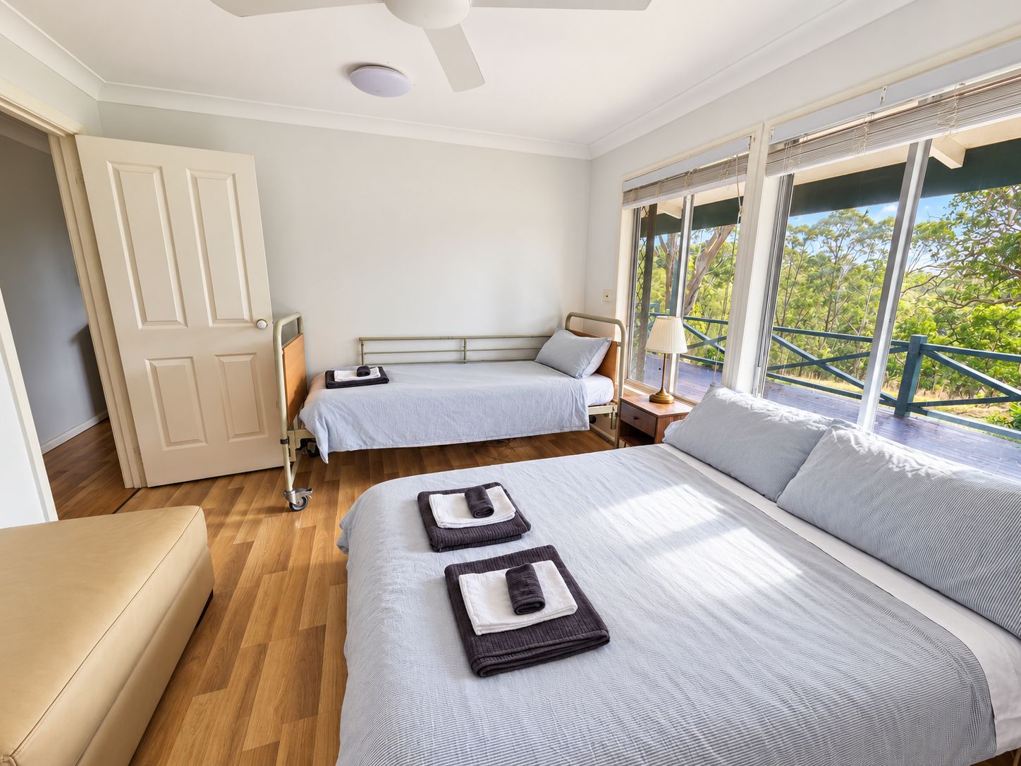 Un dormitorio con dos camas, un ventilador de techo, una ventana con vistas y una puerta.