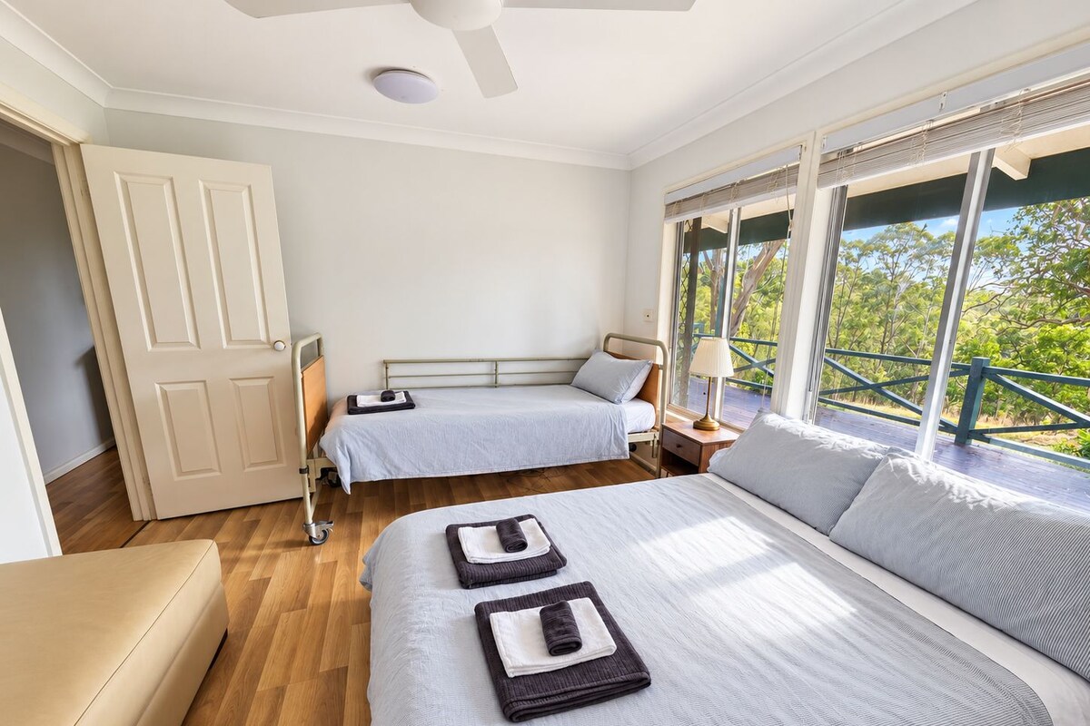 A bedroom with two beds, a ceiling fan, a window with a view, and a door.