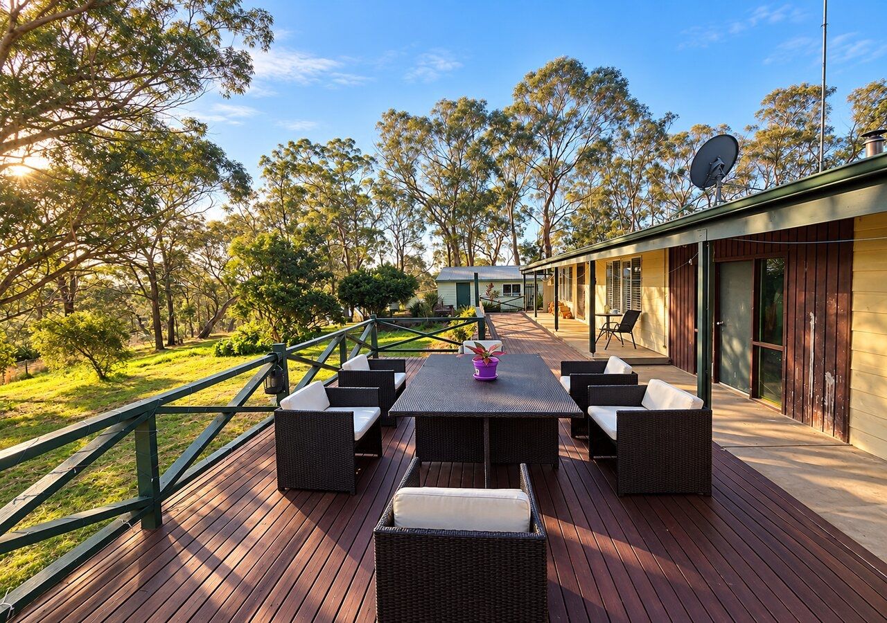 Um terraço ao ar livre com mesa e cadeiras, cercado por vegetação e árvores.