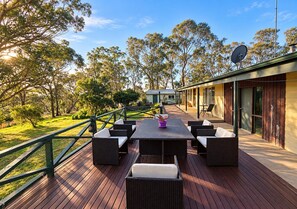 An outdoor deck with a dining table and chairs, surrounded by greenery and trees. - Private rooms - Maroota Retreat (Maroota)