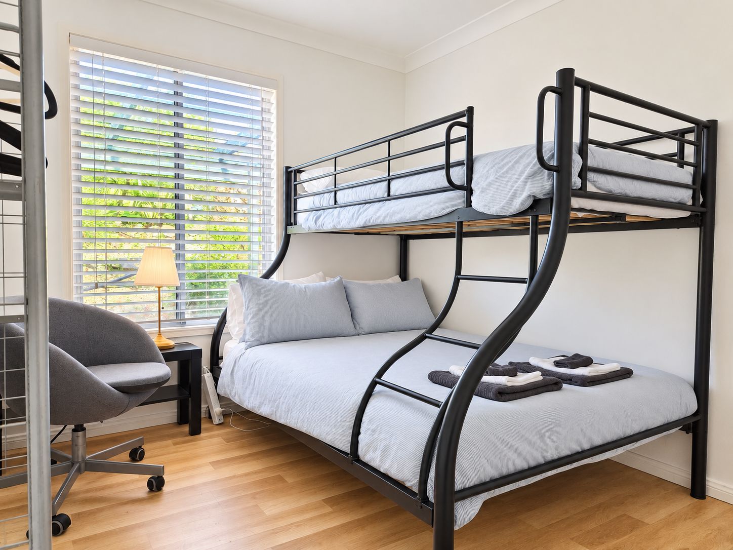 A bunk bed with a desk and chair, a window with blinds, and a lamp.