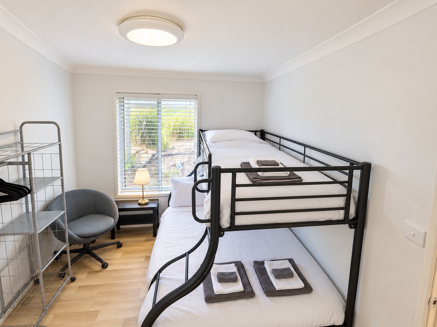 Habitación con literas, un escritorio, una silla, una ventana con persianas y una lámpara sobre el escritorio.