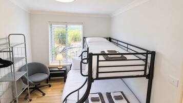 Habitación con literas, un escritorio, una silla, una ventana con persianas y una lámpara sobre el escritorio.