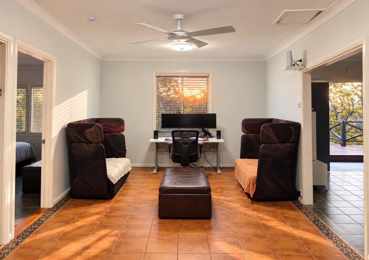 A room with a desk, two chairs, a television, and a ceiling fan.