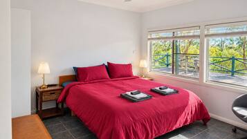 A bedroom with a bed, two bedside lamps, a nightstand, a bench, and a window with a view of greenery.