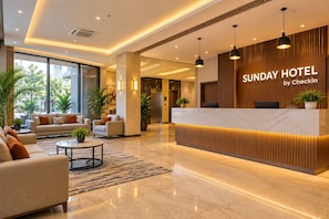 Zona de recepción de un hotel con diseño moderno, que incluye un mostrador de recepción, una sala de estar con sofás y plantas en macetas.