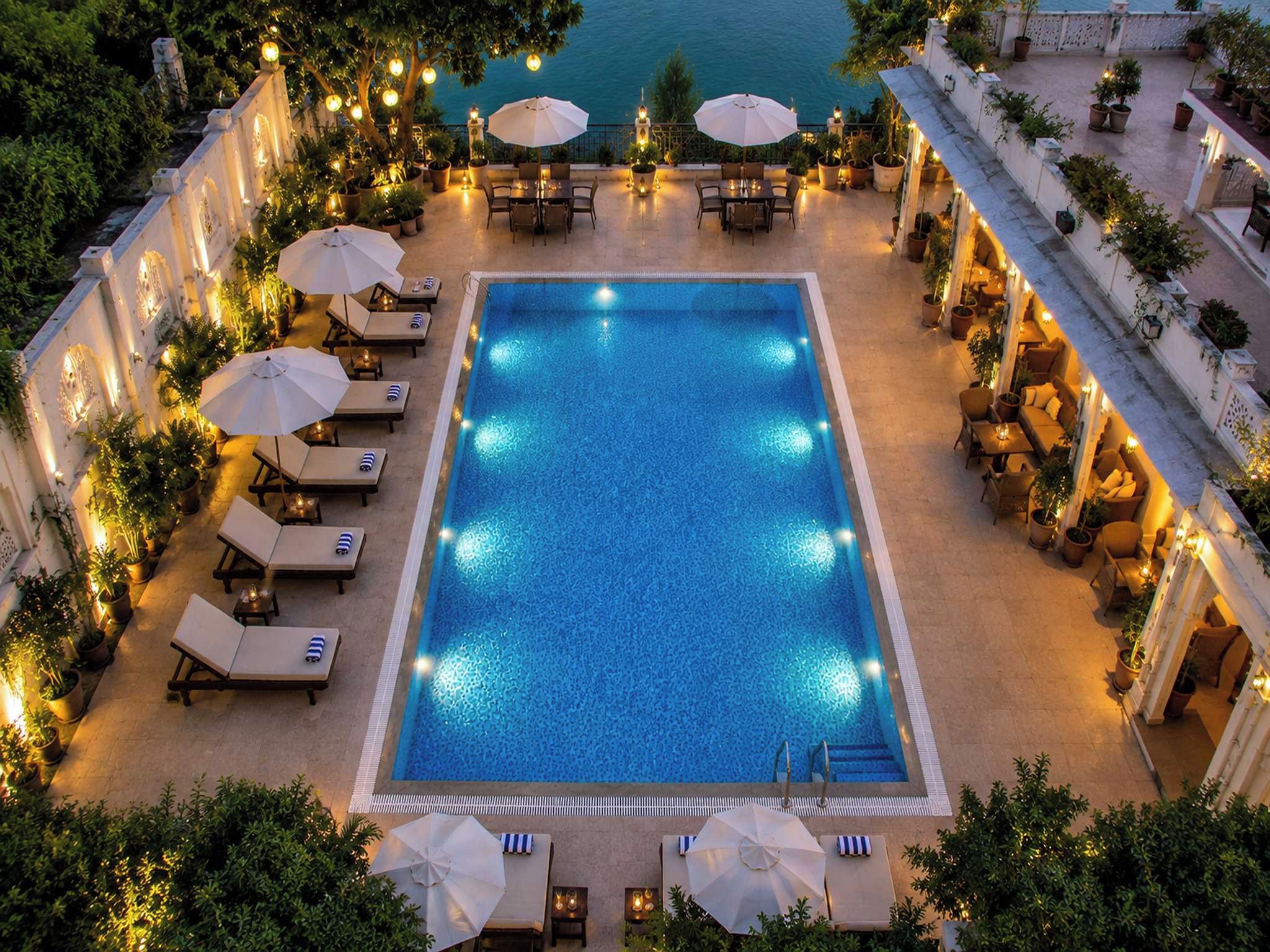 A rooftop pool with lounge chairs and umbrellas, surrounded by potted plants and a view of the sea.