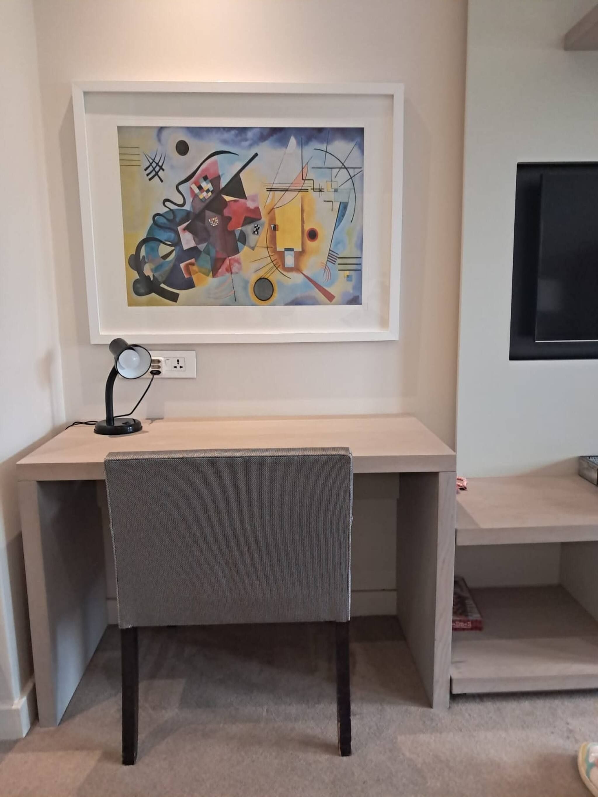 Un espacio de trabajo con escritorio, silla y un cuadro abstracto enmarcado.