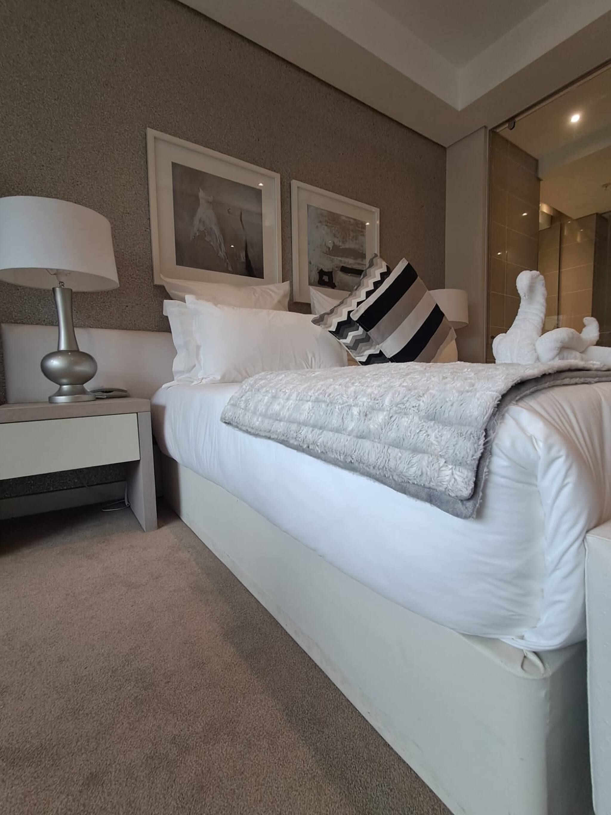 Una habitación de hotel con una cama, una mesita de noche, una lámpara y dos cuadros en la pared.
