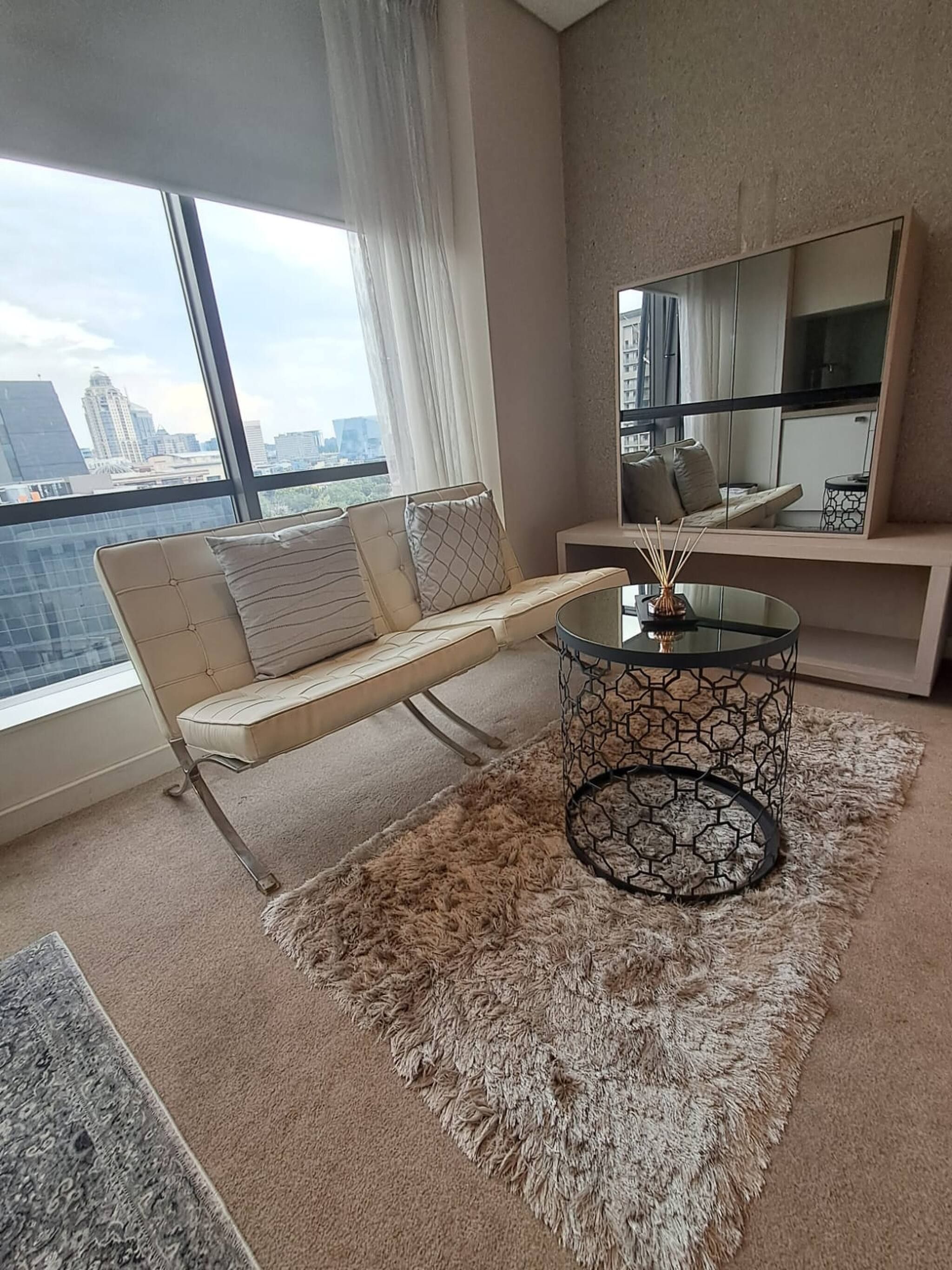Una sala de estar moderna con un sofá, una mesa de centro de vidrio y un ventanal con vistas a la ciudad.