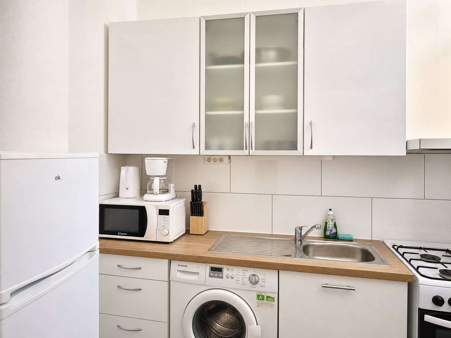 Una cocina moderna con armarios blancos, un lavavajillas Bosch, un microondas, una cafetera y un lavabo.