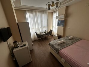 Quarto de hotel com cama, escrivaninha, cadeira, televisão e janela com cortinas.