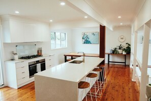 A modern kitchen with white cabinetry, a central island with stools, and a view of the outdoors. - The Perfect Family & Furry-Friend Getaway in Heart of Charlestown (Charlestown)