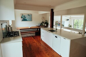A modern kitchen with a wooden floor, white cabinetry, a gas stove, and a large window providing natural light. - The Perfect Family & Furry-Friend Getaway in Heart of Charlestown (Charlestown)