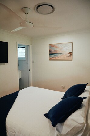 A bedroom with a bed, pillows, a ceiling fan, a painting on the wall, and a door leading to another room. - The Perfect Family & Furry-Friend Getaway in Heart of Charlestown (Charlestown)