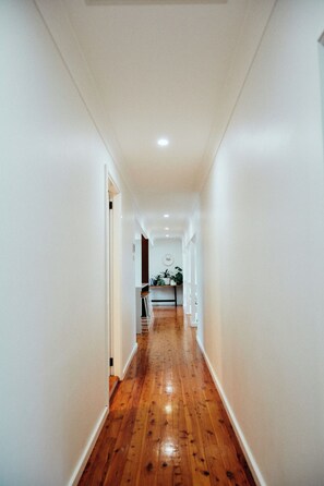 A narrow hallway with wooden flooring and white walls, leading to a room with a ceiling light. - The Perfect Family & Furry-Friend Getaway in Heart of Charlestown (Charlestown)